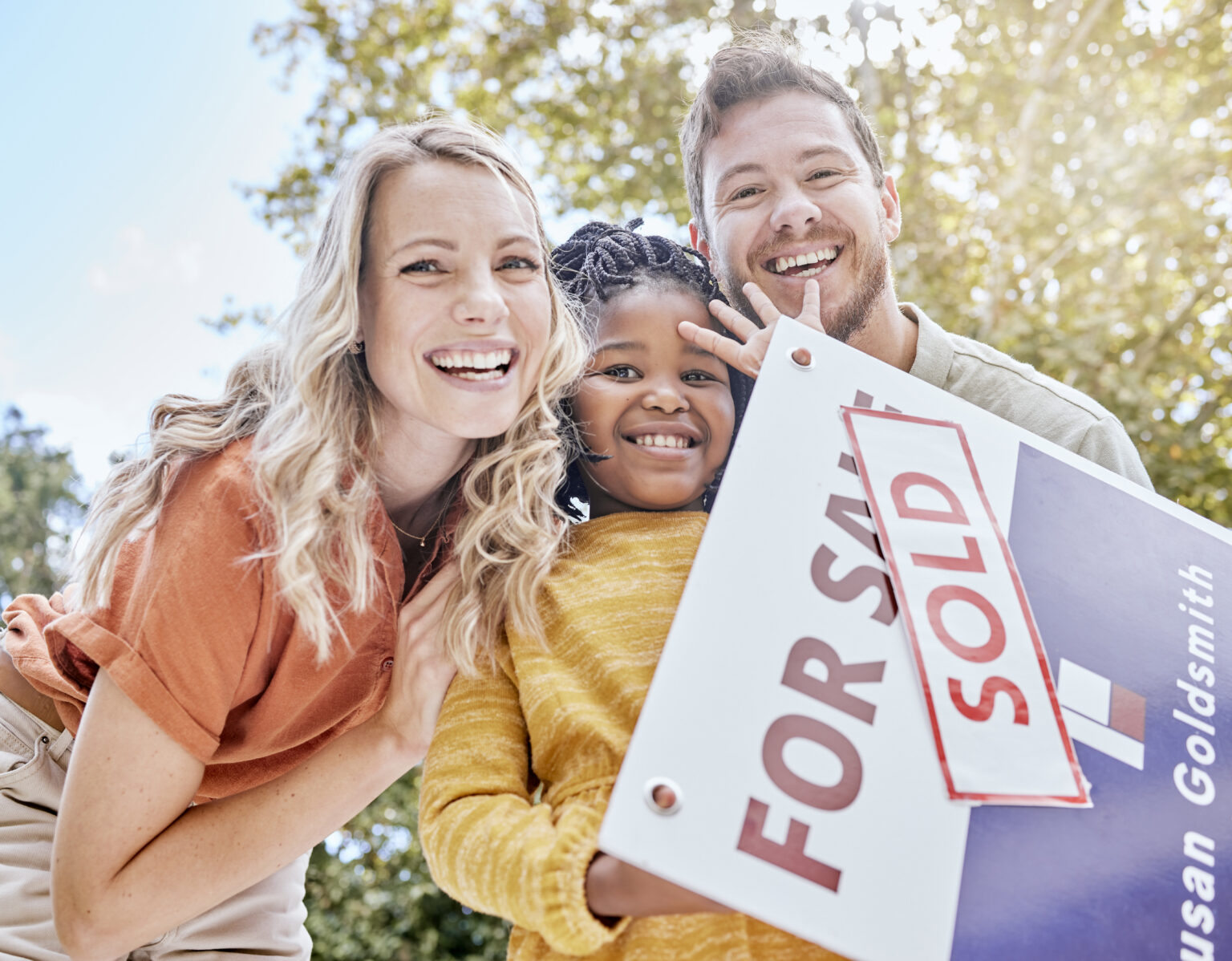 Family, adoption and homeowner with a girl and foster parents holding a sold sign in their garden o.