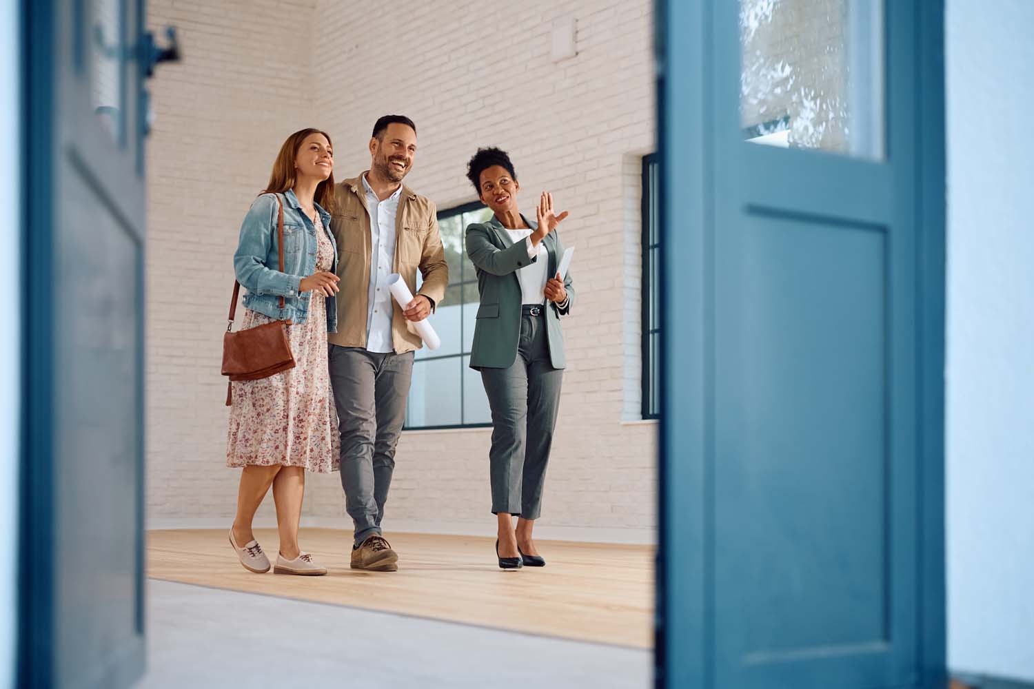 Happy African American real estate agent showing a house for sale to a couple interested in buying it. Copy space.